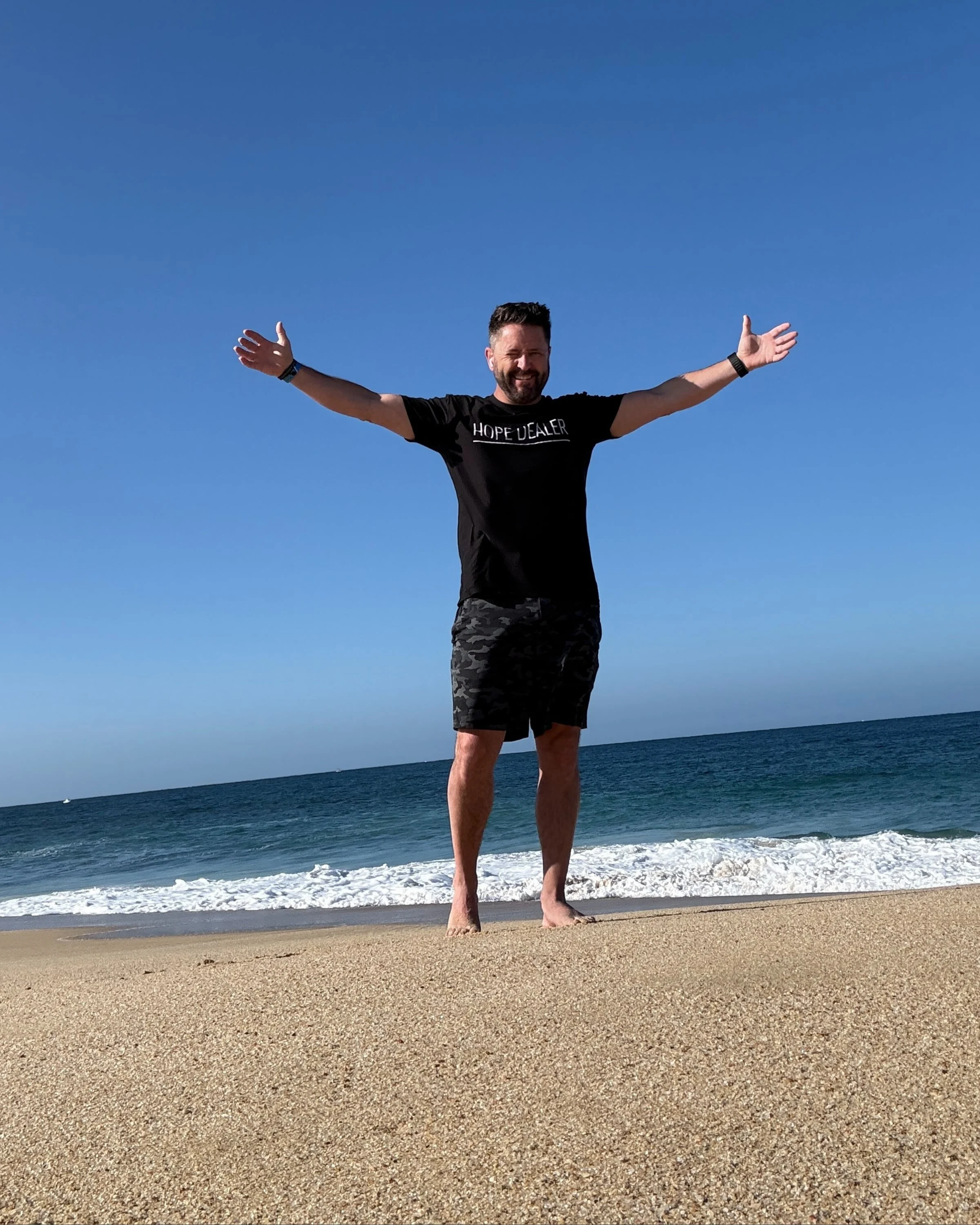 Wayne Salmans standing with arms outstretched on a beach